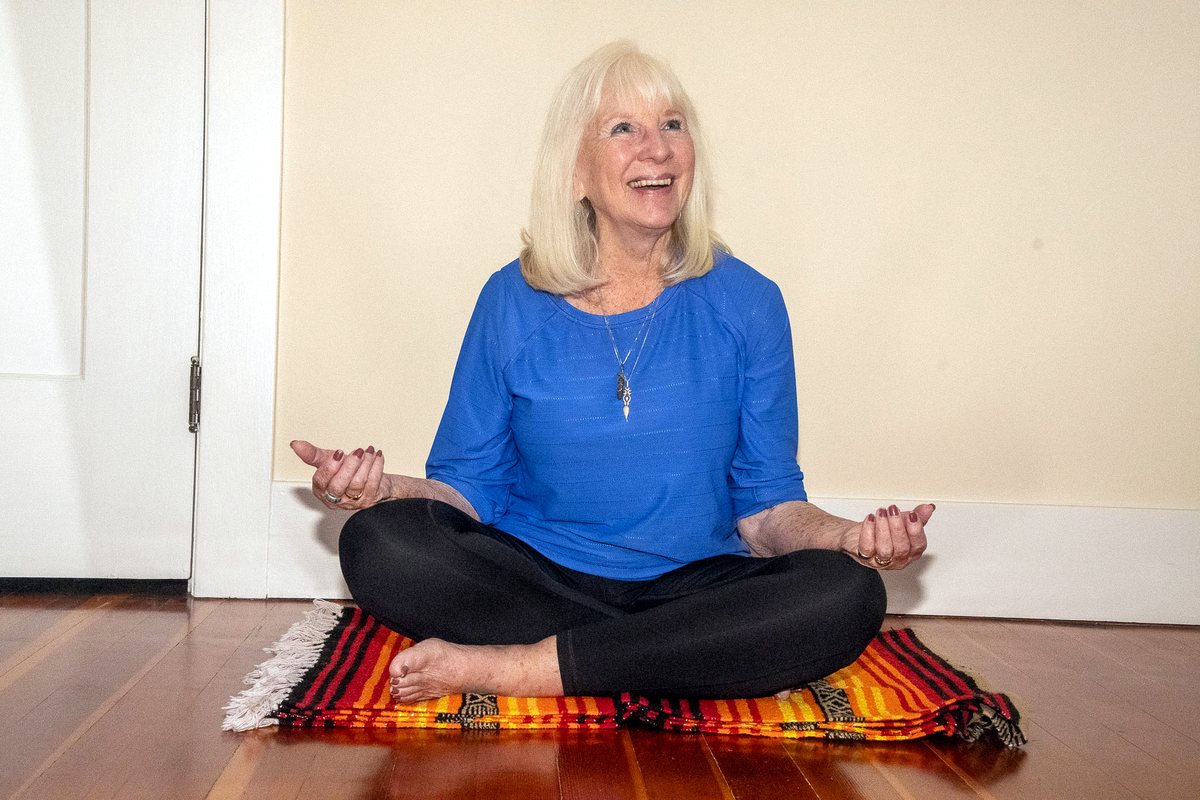 A student seated cross-legged on a mat, smiling mid-movement during a somatics session